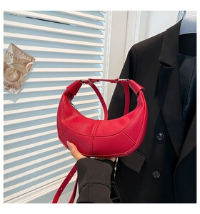Detail of red crescent leather bag showing litchi grain texture and silver metal buckle
