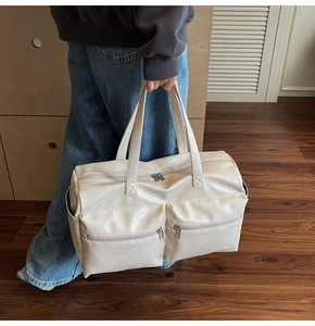 Close-up of a large cream white travel tote bag with double handles and front zipper pockets