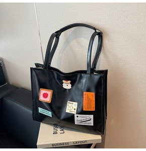 Detail of black tote bag featuring colorful graffiti patches and stylish artistic labels