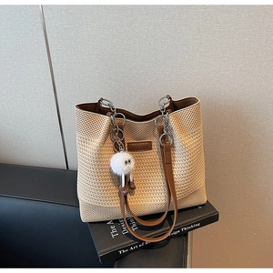 Détail d'un sac de plage en tricot avec des lanières en cuir brun et un pompon blanc
