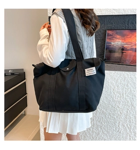 Detailed side view of a large black canvas tote bag with a white fabric patch and strap