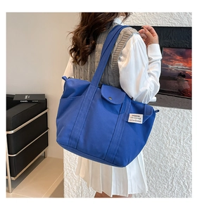 Blue canvas tote bag showing the side view on a shoulder in a modern indoor setting
