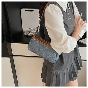 Dettaglio della borsa sottobraccio in denim blu con borchie argentate e bordo in cuoio