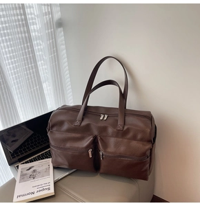 Detail of dark brown leather travel tote bag with two front zipper pockets and long straps