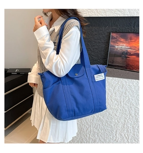 Detail of royal blue canvas tote bag featuring an outer snap pocket and fashion label