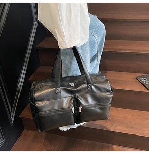 Close-up of black leather travel tote with multiple pockets on a wooden staircase