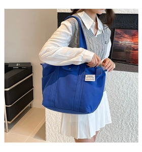 Detail of blue canvas tote bag featuring side pocket and white brand label for college