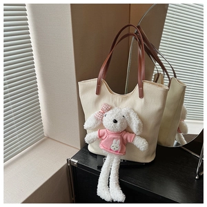 Dettaglio di una borsa tote in tela crema con manici marroni e un peluche di coniglio