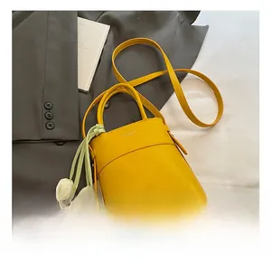 Detail of yellow pebbled leather bucket bag with white tulip charm and thin strap