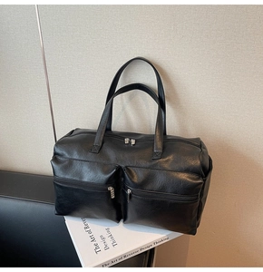 Detail view of black faux leather travel bag with dual front zipper pockets on white books