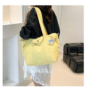 Detail of bright yellow canvas tote bag featuring front flap pocket and fashion label tag