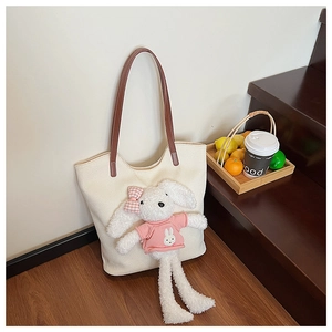 Dettaglio della borsa tote beige con manici in pelle marrone e ciondolo a coniglietto