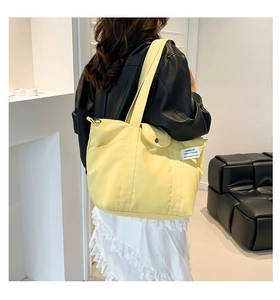 Detail of yellow canvas tote bag featuring side pocket and woven label for daily use