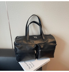 Detail of matte black leather travel tote showing symmetrical front zipper pockets and texture
