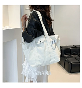 Detail view of large white canvas tote bag with snap pocket and branded woven label