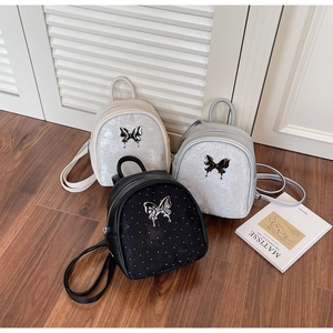 Vista de detalle de mini mochilas de mariposa en crema, plata y negro con herrajes de metal