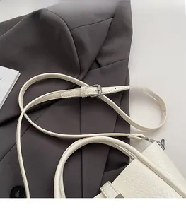 Detail of adjustable silver buckle and lychee grain texture on a white PU leather bucket bag