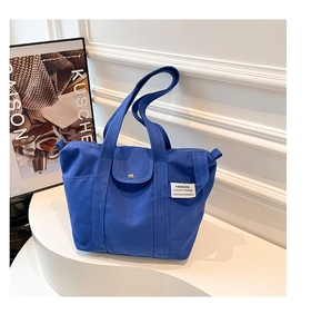 Detail of royal blue canvas tote bag featuring front snap pocket and woven brand label