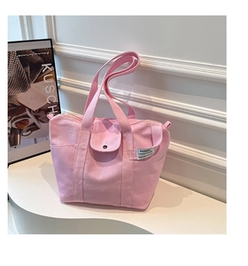 Detail of pink canvas tote bag featuring small front pocket and woven label on white podium