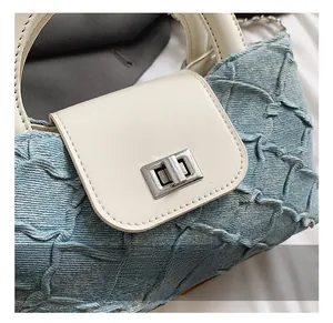 Detail des silbernen Drehverschlusses an einer hellblauen Jeans-Tasche mit weißem Lederdeckel