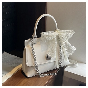 Détail d'un sac à main blanc en cuir verni avec chaîne argentée et nœud en dentelle