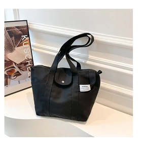 Detail of black canvas tote bag showing front pocket with flap and fashion woven label