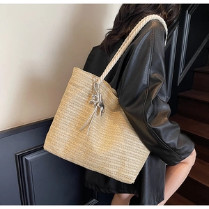 Detail of hand-woven straw tote bag featuring white rope handles and a silver star charm