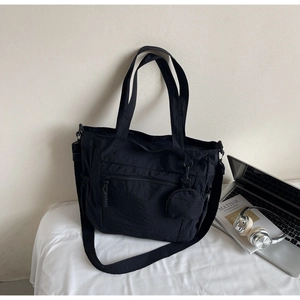 Detail of black nylon tote bag featuring front zipper pocket and detachable round pouch