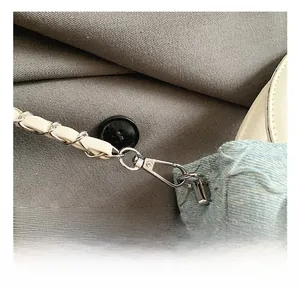 Nahaufnahme von silbernem Karabiner und weißer Lederkette an einer blauen Tweed-Tasche