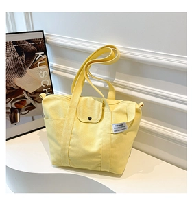 Close-up of pale yellow canvas tote bag with flap snap closure and side pocket detail