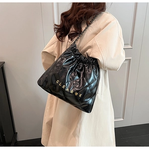 Detail of black quilted leather drawstring bucket bag with gold chain strap on model