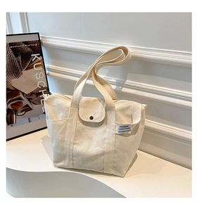 Close-up of cream canvas tote bag with front pocket, magnetic buckle and woven label