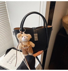 Detail of black pebbled leather bucket bag with silver lock and plush bear charm