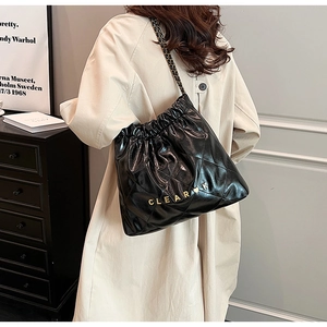 Detail of black quilted leather bucket bag with gold chain strap worn by a model