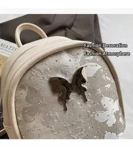 Détail du mini sac à dos crème avec texture papillon et embellissements de clous en métal