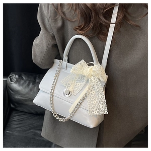 Détail du sac bandoulière gris clair avec chaîne argentée et nœud en dentelle