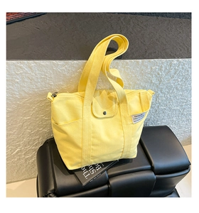 Detail of a bright yellow canvas tote bag with front pocket and side storage pocket