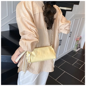 Detail of light yellow ruched baguette bag with long white fringes and silver chain strap