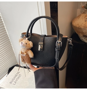 Detail of black litchi grain bucket bag featuring a silver lock and cute bear charm