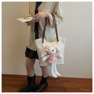 Dettaglio della borsa tote in tela beige con un peluche a forma di coniglio sulla modella