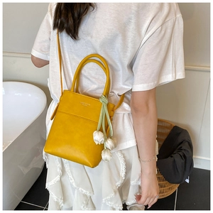 Detail of yellow mini tote bag with tulip pendant and logo shown in lifestyle setting