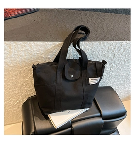 Detail of black canvas tote bag with woven label and metal buckle on woven seat