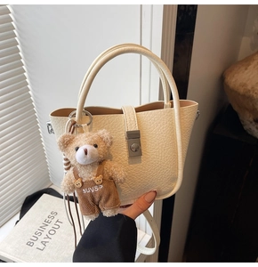 Close-up of cream white lychee texture leather bag with silver buckle and plush bear charm