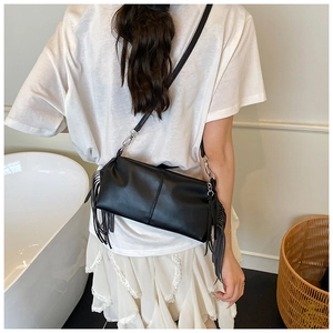 Detail showing side tassels and silver metal hardware of the black pleated crossbody bag