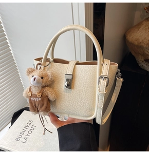 Close-up of beige lychee leather bucket bag with silver hardware and a cute bear charm