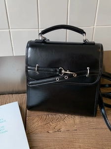 Minimalist black patent leather backpack with top handle and metallic buckle details