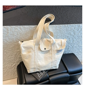 Detail showing cream canvas tote bag with snap-button flap, side pocket, and black zipper closure