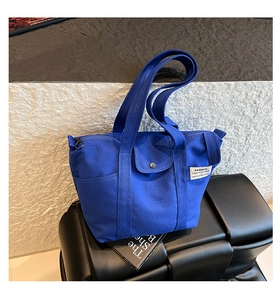 Detail of blue canvas tote bag featuring double straps and metal ring zipper closure