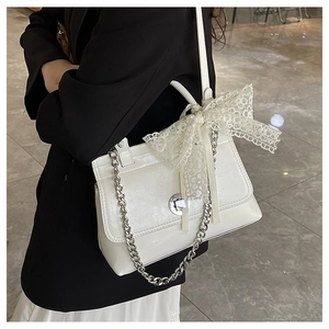 Détail d'un sac cabas blanc brillant avec nœud en dentelle et bandoulière chaîne argent