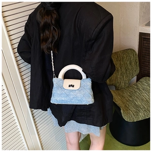 Details einer blauen Denim-Stepptasche mit cremefarbenem Ledergriff und gewebtem Gurt